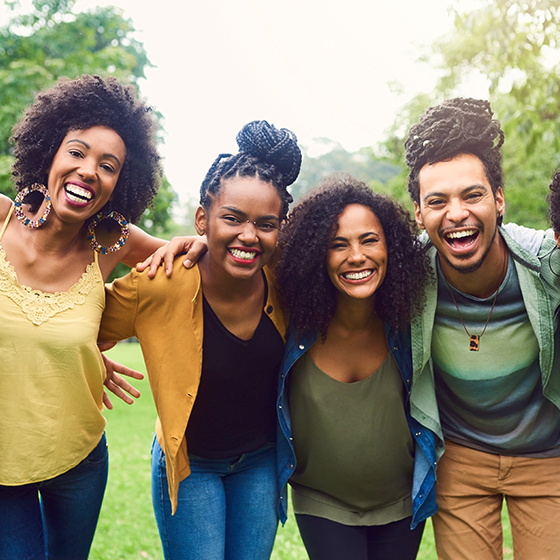 Quatro jovens negros, lado a lado, sendo dos homens e duas mulheres, sorriem alegremente abraçados